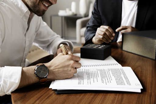 a male real estate agent smiling while signing a contract with another agent